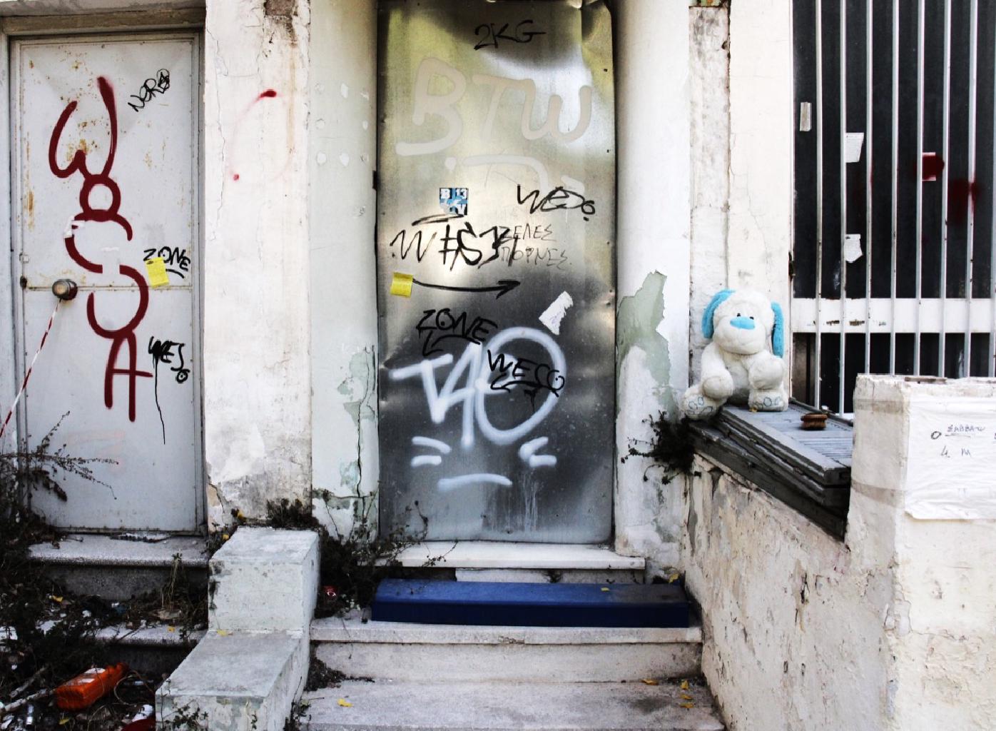 Κι εδώ το φαινομενικά σκληρό και αποκλειστικά αστικό γίνεται οικείος χώρος μ’ ένα λούτρινο πανέμορφο σκυλάκι. Μια σκηνογραφία απλή, μια άλλη τοποθέτηση ενός όμορφου αντικειμένου ζωογονεί και ψυχώνει όλον τον μεταλλικό κόσμο. Λες και μια παιδική ηλικία, η παιδική ηλικία του καθένα, μας χαιρετάει και αίφνης γινόμαστε πάλι τρυφεροί. Ακόμη και ένα μικροσκοπικό Playmobil είναι αρκετό έστω σαν απομεινάρι ενός χώρου που κάποτε φιλοξενούσε κόσμο για να θυμίσει ακριβώς αυτή τη ζωή. Ή μήπως το σκυλάκι είναι ο θάνατος που συνέβη στα χαμόσπιτα της φωτογραφίας; Ναι, αυτό συμβολίζει το σκυλάκι. Μια κάποια ζωή που κάποτε ήχησε πριν να κατασιγαστεί για πάντα.